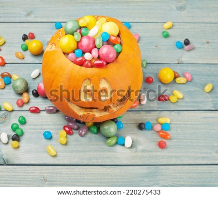 Jack o lantern halloween pumpkin filled with multiple colorful sweets and candies over the wooden board background composition