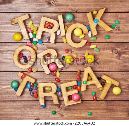 Trick or treat written with wooden letters and multiple candy sweets lying around over the covered with brown boards surface composition