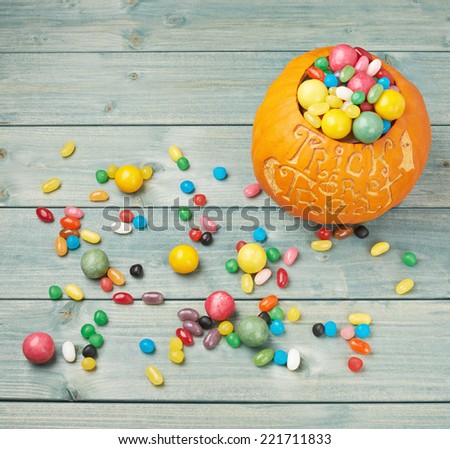Halloween pumpkin with the words trick or treat carved over its surface and filled with multiple sweets and candies, composition over the wooden board background