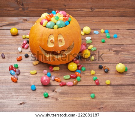 Jack o lantern halloween pumpkin filled with multiple colorful sweets and candies over the wooden board background composition