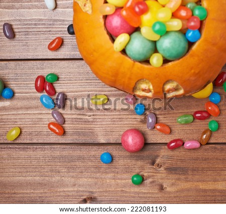 Jack o lantern halloween pumpkin filled with multiple colorful sweets and candies over the wooden board background composition, top view above foreshortening