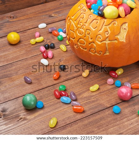 Halloween pumpkin with the words trick or treat carved over its surface and filled with multiple sweets and candies, composition over the wooden board background