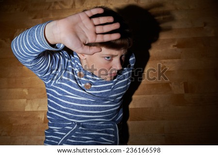 Child abuse composition of a frightened young boy sitting on the wooden floor in a light of a flashlight circle