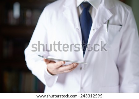 Close-up fragment of a man in a white doctor\'s coat holding a pad tablet device in his hands, shallow depth of field composition