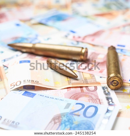 Few ammunition bullet shells over the surface covered with the multiple euro bank note bills, shallow depth of field composition