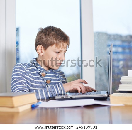 Concentrated undistracted 12 years old children boy sitting at the wooden desk against the notebook compouter, composition against the window
