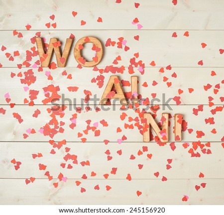 Wo Ai Ni meaning I Love You in Chinese written with the block letters covered with red heart shaped confetti over the wooden background