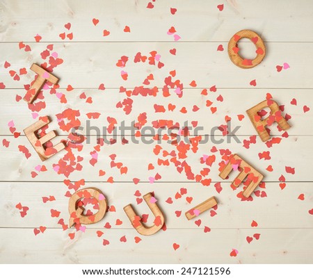 Te Quiero meaning I Love You in Spanish written with the block letters covered with red heart shaped confetti over the wooden background