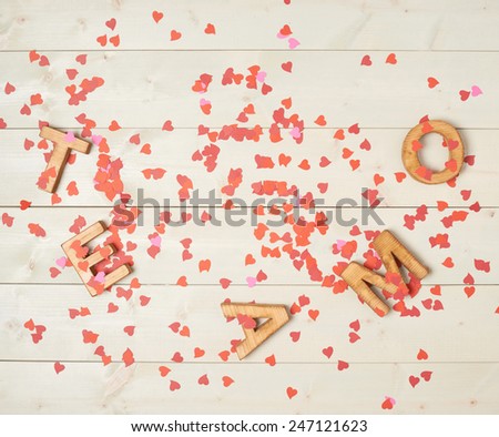 Te Amo meaning I Love You in Spanish written with the block letters covered with red heart shaped confetti over the wooden background