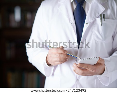 Close-up fragment of a man in a white doctor\'s coat writing down something in a notebook with a pencil, shallow depth of field composition
