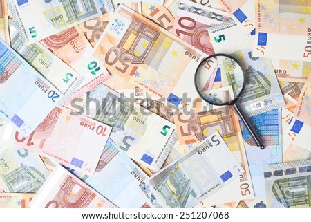 Magnifying glass over the surface covered with multiple euro bank note bills