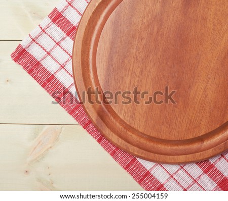 Red tablecloth or towel over the surface of a wooden table with a round wooden tray on top of it