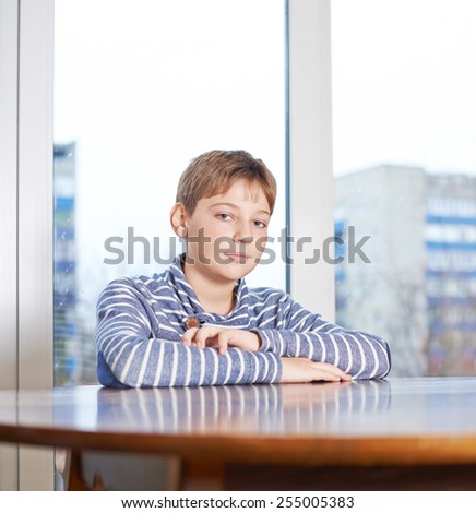 12 years old childen boy sitting still at the wooden desk, composition against the window