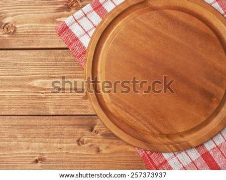 Red tablecloth or towel over the surface of a brown wooden table with a round wooden tray on top of it