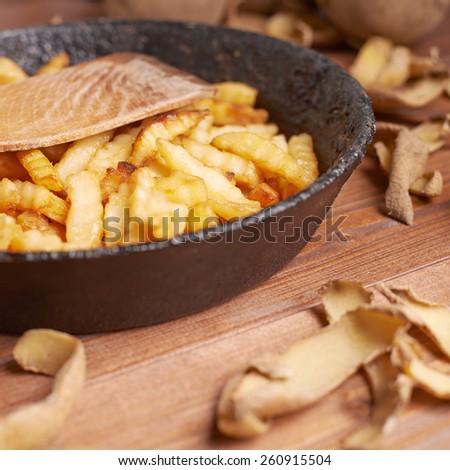 Cooking fried french potatoes composition of an old iron pan, potatoes, peels and pile of fries over the wooden table\'s surface