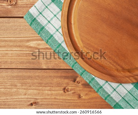 Green tablecloth or towel over the surface of a brown wooden table with a round wooden tray on top of it