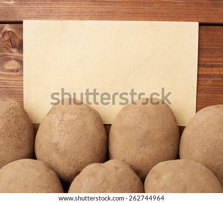 Pile of earth dirty potatoes lying against the copyspace brown piece of paper, composition over the wooden table\'s surface
