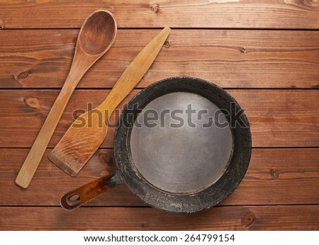 Cooking composition of the old frying pan, wooden spatula and spoon over the table's surface