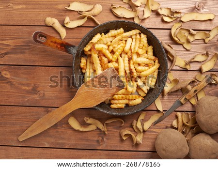 Cooking fried french potatoes composition of an old iron pan, potatoes, peels and pile of fries over the wooden table\'s surface