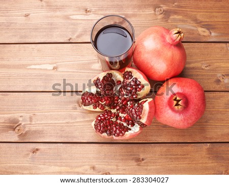 Pomegranate Punica granatum fruit next to the tall glass full of red juice, composition placed over the wooden boards surface