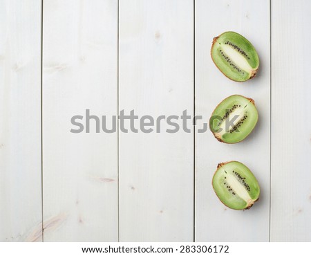 Three sliced halves of kiwifruit or chinese gooseberry kiwi over the white wooden board surface