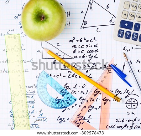 Studying math back to school composition of the green apple and some stationery office supplies lying over the sheet filled with trigonometry equations and formulas