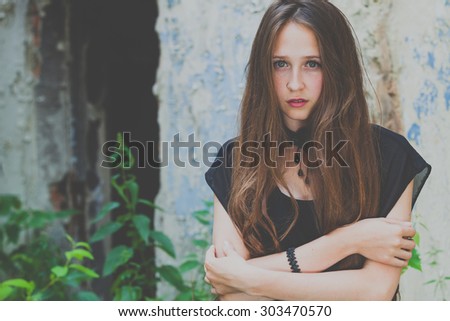 portrait of a beautiful young sad goth girl in an abandoned old building outdoors at the day time