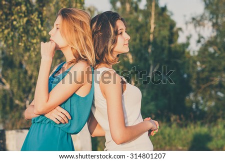 Pretty beautiful brunette and blonde girl friends having fun. Both standing in park and smiling (laughing). Concept of female friendship.