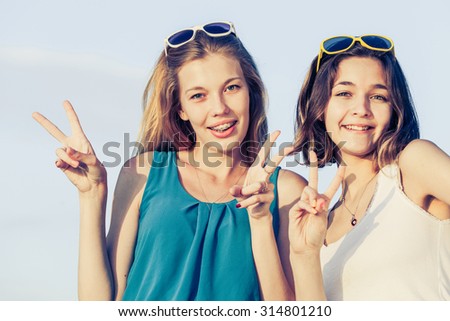 Pretty beautiful brunette and blonde girl friends having fun. Both standing in park and smiling (laughing). Concept of female friendship.