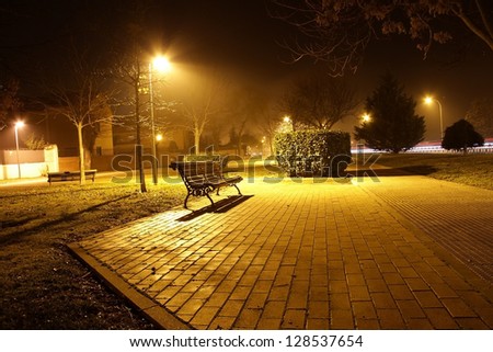 Night view of a park bench in the pool of light cast by a street light in autumn