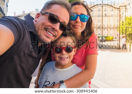 Family having fun wearing sunglasses & waving to a camera taking selfie photograph on summer holiday