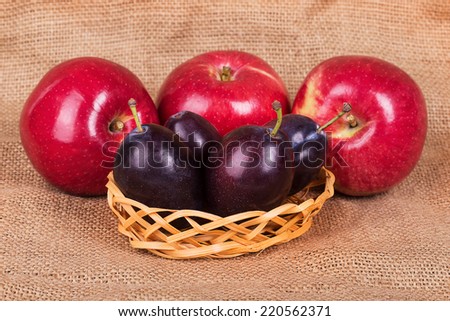 Three red apples and four plums on background of sacking