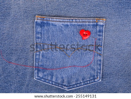 Red heart shaped button with needle and red thread on denim fabric