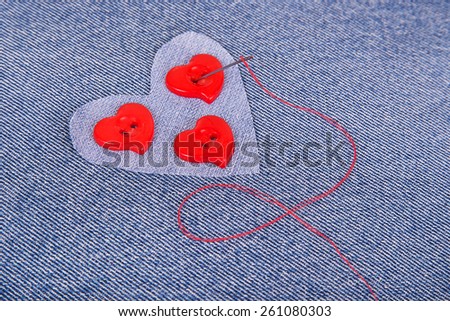 Red heart shaped buttons with needle and red thread on denim fabric