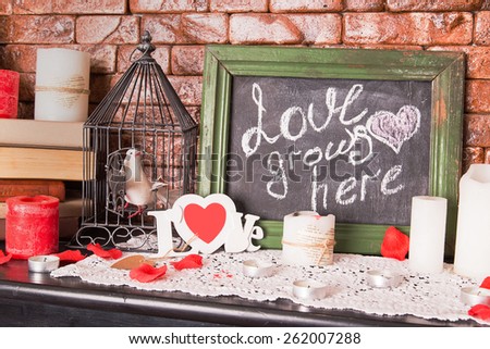 Close up of a black dirty board with the words Love grows here with candles on shelf