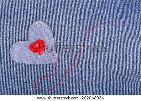 Red heart shaped button with needle and red thread on denim fabric