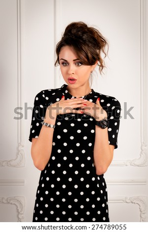 Portrait of a shocked sexy woman in a black dress on light background in studio