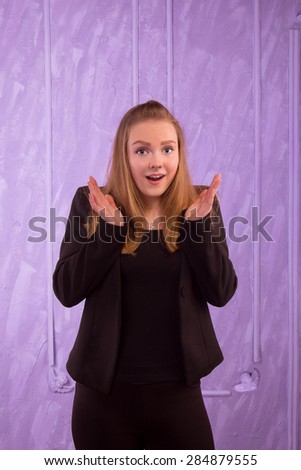 Portrait of a surprised young woman in a black suit on a purple background