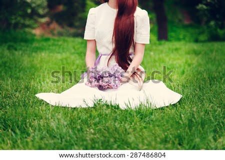Woman in wedding dress sitting on the grass and holding a bouquet of lilacs