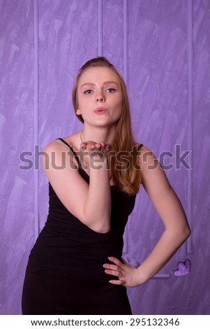 Young woman in black sends a kiss on a purple background