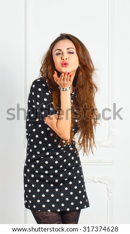 Young attractive woman in black dress sends a kiss in the studio
