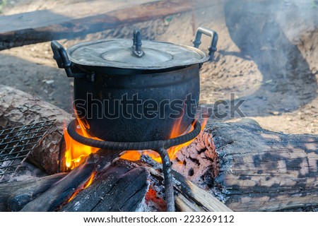 black pot boiling water for cooking on the fired stove next to firewood pile, Thailand Esan traditional culture ancient method