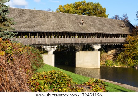 Wooden covered bridge, also known as Zehnders Holz Brucke, spans the Cass River in Frankenmuth Michigan. Warm autumn colors surround the wooden bridge.