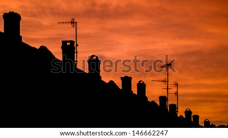 Terraced house silhouette with chimneys and areal antennas on a dramatic evening sky