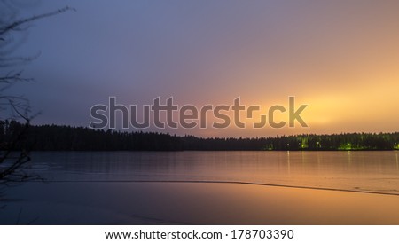 icy lake at night in sweden with light pollution from nearby city,