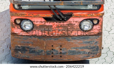 front of a funny looking small rusty car which like a anthropomorphic face of a robotic cartoon character