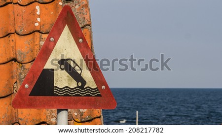 Old harbor sign warning you not to drive your classic car over the edge and plunge down into the water.  Can be used to illustrate the Wall Street Crash of 1929 since the car depicted is from that era