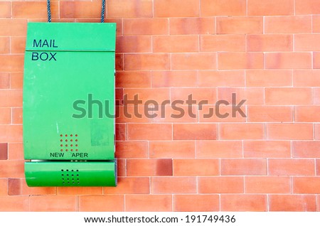 Green mailbox against red brick wall.