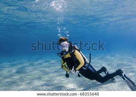 Female scuba diver over white sand in clear blue water