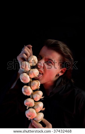 Evil vampire with scary eyes is licking garlic, red horror light, isolated on black background